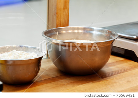 Stainless steel bowl with flour on a wooden table 76569451