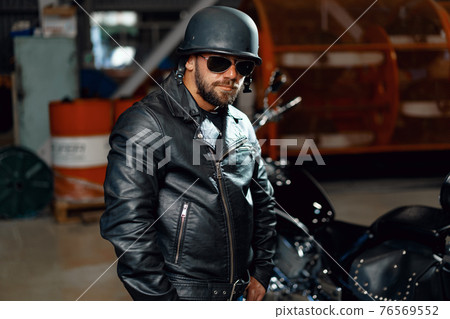 Portrait of bearded man motocyclist in dark sunglasses on dark background Portrait of bearded man motocyclist in dark sunglasses on dark background 76569552