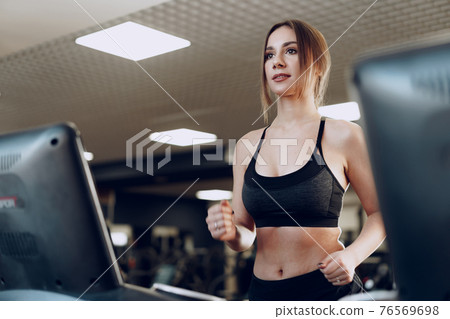 Pretty fit woman in black sportrswear training on a treadmill Pretty fit woman in black sportrswear training on a treadmill 76569698