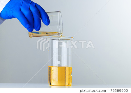 Scientist or doctor in blue gloves pouring some yellow liquid into a flask 76569900