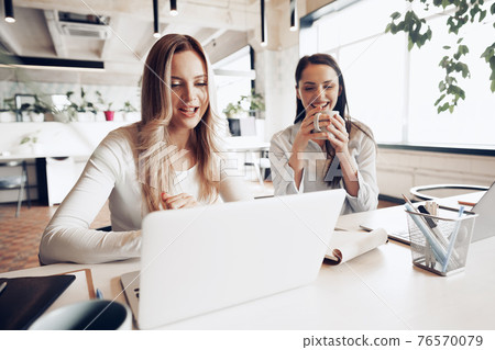 Two young female colleagues discussing business project together in office 76570079