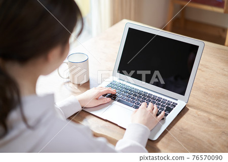 Back view of an Asian woman working on a computer in the living room 76570090