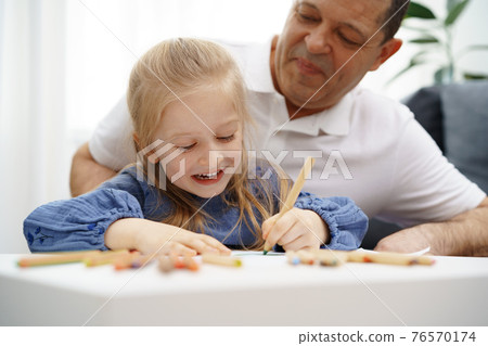 Grandfather and granddaughter drawing together in living room Grandfather and granddaughter drawing together in living room 76570174