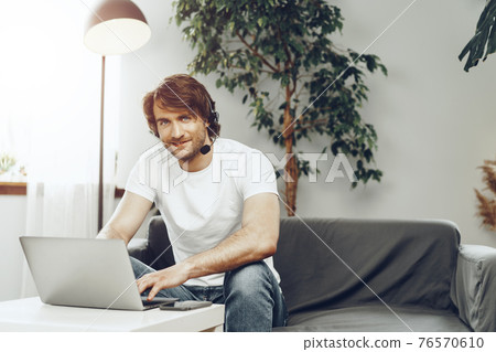 Young man businessman with headset working on laptop from home 76570610