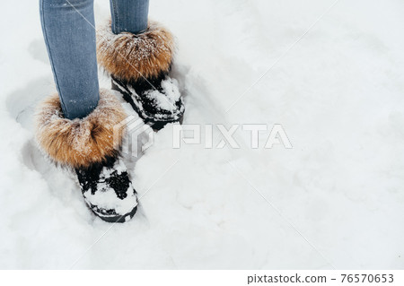 Female legs wearing jeans and warm furry boots standing in a snow 76570653