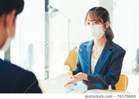 A woman in a mask serving customers through an acrylic board A woman in a mask serving customers through an acrylic board 76570669