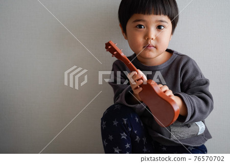 Three-year-old child holding a toy guitar Three-year-old child holding a toy guitar 76570702