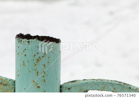 A rusty metal pipe sticks out over an iron fence. 76571340