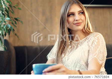 Nice young woman enjoying cup of coffee in a coffee shop Nice young woman enjoying cup of coffee in a coffee shop 76571604
