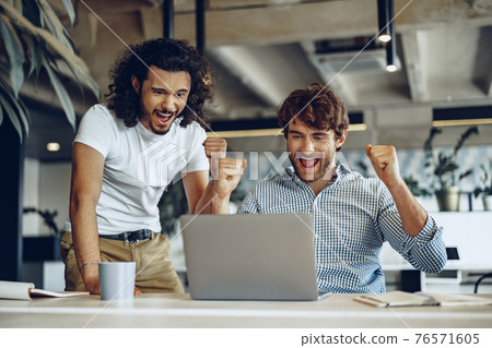 Two excited overjoyed young businessmen looking at laptop screen happy to win or recieved good news 76571605