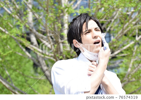 A young man who is hot and removes his mask and wipes his sweat with a handkerchief 76574319