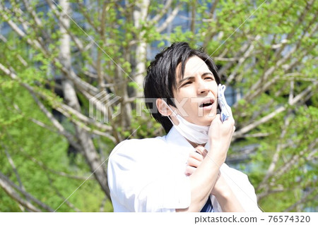 A young man who is hot and removes his mask and wipes his sweat with a handkerchief A young man who is hot and removes his mask and wipes his sweat with a handkerchief 76574320