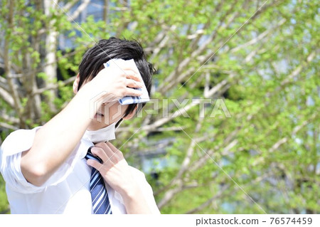 一個熱的年輕人摘下口罩用手帕擦汗 一個熱的年輕人摘下口罩用手帕擦汗 76574459