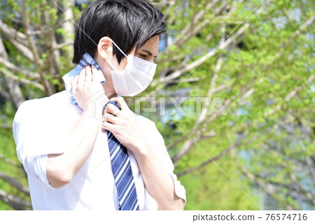 A young man wiping his sweat with a handkerchief due to the stuffiness of his mask A young man wiping his sweat with a handkerchief due to the stuffiness of his mask 76574716