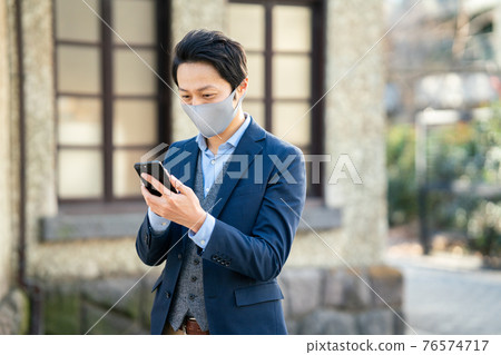 A man wearing a mask outside and looking at a smartphone 76574717