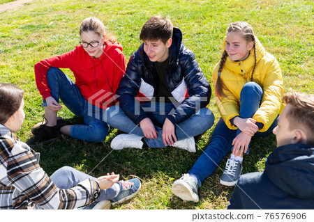 Cheerful teens sitting on green lawn and talking 76576906