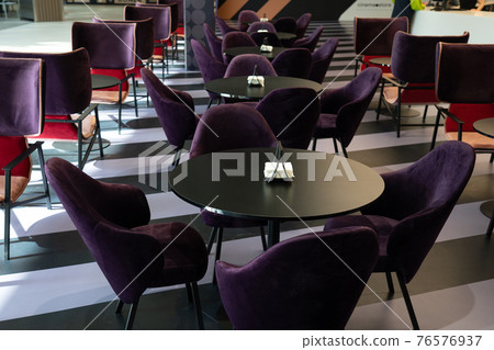 A row of tables with soft comfortable violet chairs for visitors to the food court of a modern shopping center. 76576937