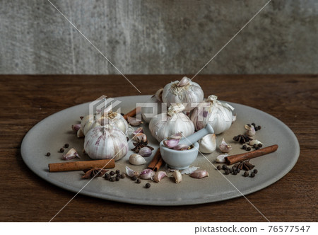 Garlic bulbs and Garlic cloves with Herbs spices, Cinnamon, Star anise and Pepper grain in Ceramic plate on Wooden rustic table. Garlic bulbs and Garlic cloves with Herbs spices, Cinnamon, Star anise and Pepper grain in Ceramic plate on Wooden rustic table. 76577547
