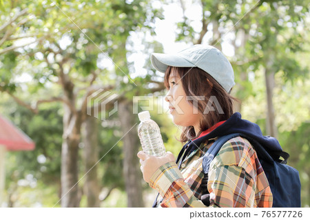 A woman climbing a mountain wears a hat, carries a backpack and keeps hydrated 76577726