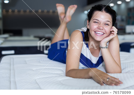 Female is happy lying on new mattress in the store 76578099