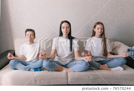 mother daughter and son are sitting on the sofa in the lotus position engaged in meditation. 76578244
