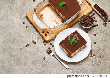 Traditional Italian Tiramisu dessert in glass baking dish and portion on grey concrete background Traditional Italian Tiramisu dessert in glass baking dish and portion on grey concrete background 76578581