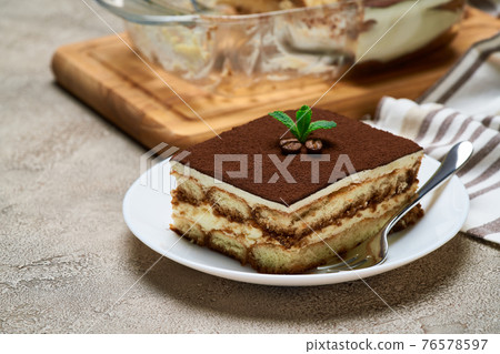 Traditional Italian Tiramisu dessert in glass baking dish and portion on grey concrete background 76578597