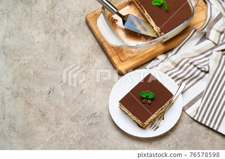 Traditional Italian Tiramisu dessert in glass baking dish and portion on grey concrete background 76578598