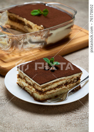 Traditional Italian Tiramisu dessert in glass baking dish and portion on grey concrete background 76578602