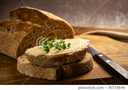 sliced toast bread with butter on wooden cutting board with knife 76578646