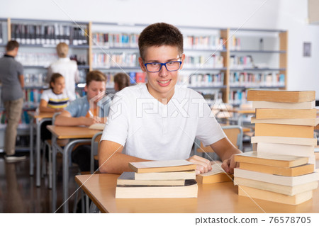 Schoolboy sitting with stacks of books in school library Schoolboy sitting with stacks of books in school library 76578705