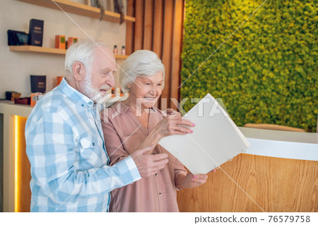 Gray-haired couple standing near reception in a spa center and looking trhough the price list Gray-haired couple standing near reception in a spa center and looking trhough the price list 76579758