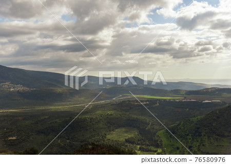 A view of a mountain range and a green valley in the morning at sunrise, against a dramatic back of blue skies and clouds. High quality photo. Travel concept hiking. North District Israel A view of a mountain range and a green valley in the morning at sunrise, against a dramatic back of blue skies and clouds. High quality photo. Travel concept hiking. North District Israel 76580976