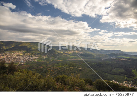A view of a mountain range and a green valley in the morning at sunrise, against a dramatic back of blue skies and clouds. High quality photo. Travel concept hiking. North District Israel A view of a mountain range and a green valley in the morning at sunrise, against a dramatic back of blue skies and clouds. High quality photo. Travel concept hiking. North District Israel 76580977