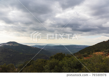 A view of a mountain range and a green valley in the morning at sunrise, against a dramatic back of blue skies and clouds. High quality photo. Travel concept hiking. North District Israel A view of a mountain range and a green valley in the morning at sunrise, against a dramatic back of blue skies and clouds. High quality photo. Travel concept hiking. North District Israel 76580978