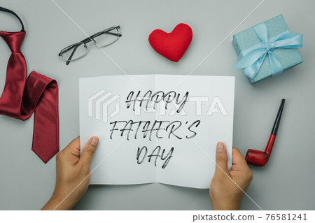 Table top view Happy Fathers day holiday background concept. Hand daddy open greeting card of season. Flat lay object gift box Smoking Cigarette red heart necktie eyeglasses on grey background. 76581241