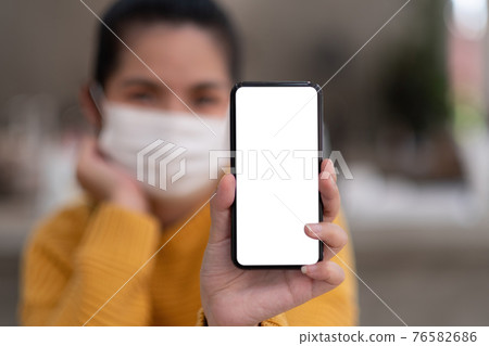 Mockup image of a beautiful woman wear mask while holding mobile phone with blank white screen. 76582686