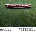 Wooden boat without people with green lake water reflection, row boat side view. 76583311