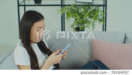 Beautiful happy woman lying on comfortable couch, typing message in social networks, using mobile application, shopping online in internet store on smartphone. Beautiful happy woman lying on comfortable couch, typing message in social networks, using mobile application, shopping online in internet store on smartphone. 76584097