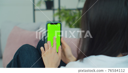 Rear view of woman in modern room sitting on couch using phone with green screen mockup Chroma Key with trackpoints surfing internet Viewing content. Rear view of woman in modern room sitting on couch using phone with green screen mockup Chroma Key with trackpoints surfing internet Viewing content. 76584112