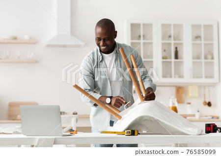 Furniture assembly. Happy african american man screwing detail to chair, looking at laptop at manual in blog Furniture assembly. Happy african american man screwing detail to chair, looking at laptop at manual in blog 76585099