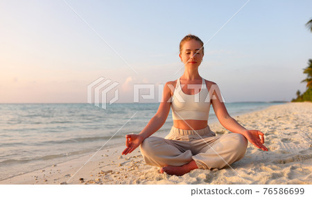 Peaceful woman meditating in Padmasana on coast 76586699