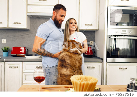 Loving couple cooking food in kitchen with their Border Collie dog Loving couple cooking food in kitchen with their Border Collie dog 76587519