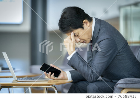 A businessman holding a smartphone holding his head A businessman holding a smartphone holding his head 76588415