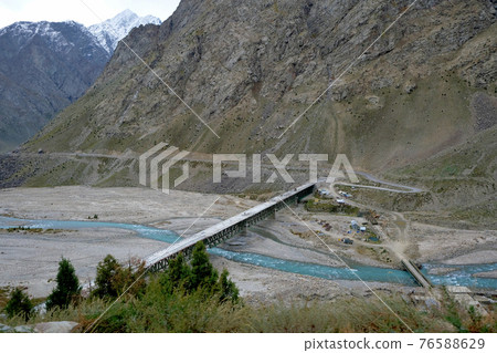 A bridge over a turquoise river in the vast snow-capped mountains of the Himalayas 76588629