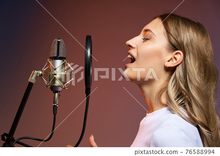 Singer girl with microphone. Closeup profile portrait of young Caucasian girl singing enjoying with closed eyes 76588994