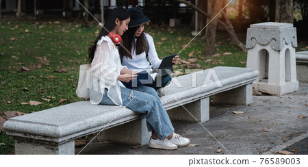 Asian woman traveler with backpack using maps on tablet and sitting in park, travel holiday relaxation concept. 76589003