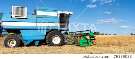 Scenic side view Big powerful industrial combine harvester machine reaping golden ripe wheat cereal field on bright summer or autumn day. Agricultural yellow field machinery landscape background 76589088