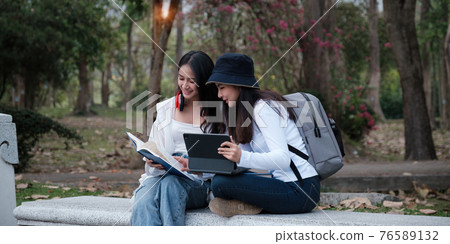 Asian woman traveler with backpack using maps on tablet and sitting in park, travel holiday relaxation concept. 76589132