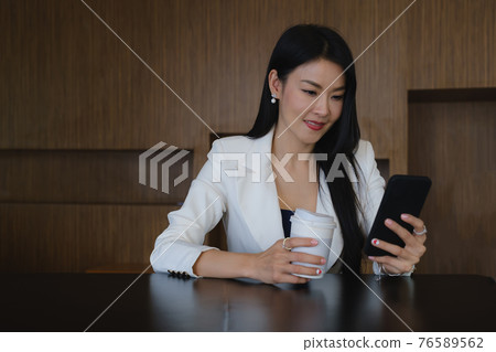 Businesswoman using mobile phone with smile and sitting at her office desk for working. Businesswoman using mobile phone with smile and sitting at her office desk for working. 76589562